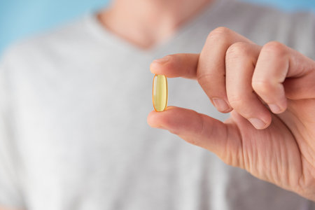 Man holding capsules with omega 3, vitamin D in hand. Nutritional supplement with fish oil. Health support and treatment concept.の写真素材