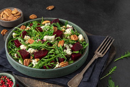 Arugula, beet and blue cheese salad with pecan nuts in a plate with fork on black table background. healthy vegetarian foodの写真素材