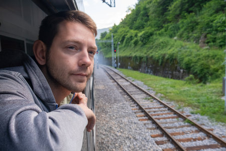 Young man looking out of train window while traveling by railway through Balkans. Male traveler looking out sleeping car window in the morningの写真素材