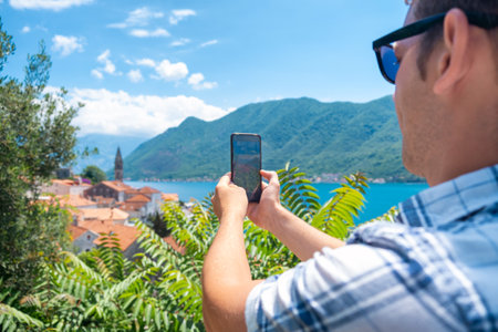 Man in sunglasses taking photo of old town Perast in Kotor bay, Montenegro. Male tourist on summer vacation taking pictures of landmark for social media. Young guy enjoying holidaysの写真素材