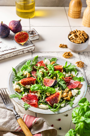 Delicious fig and prosciutto salad with arugula, cheese and walnuts in a plate on white tile background. healthy diet foodの写真素材