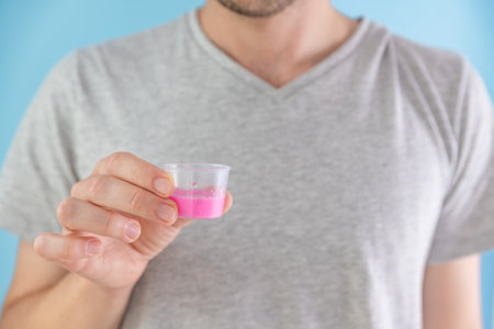Man holding gastritis, stomach ulcer, heartburn liquid medicine syrup in measuring cup. Taking medicine, health care, pharmacy and treatment conceptの写真素材