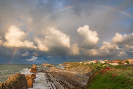 Full rainbow over sea coast with Arnia beach in Santander, Cantabria, North Spain with cliffs and flysch rocks. Popular travel destinationの写真素材
