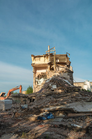 Demolition of ruined building. Excavator breaks old house damaged by terrorist attack, war or earthquake to build new house. Vertical orientationの写真素材