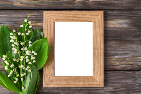 Blank photo frame with spring Lily of the valley flowers bouquet on rustic wooden background....