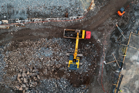 Aerial top down view of construction site with excavator and dump trucks during earthworks. Digger...