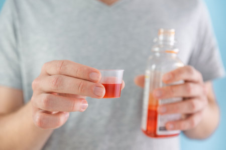 Man drinking dose of liquid medicine syrup for treatment cold and flu in measuring cup. Male taking liquid drug from meds bottle. Taking medicine, health care, pharmacy conceptの写真素材