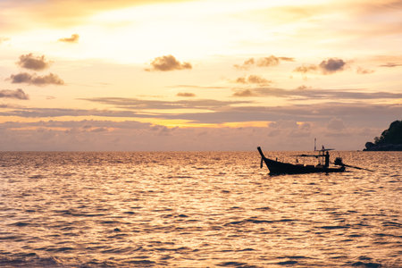 Silhouette of Thai traditional longtail boat floating on the ocean during a stunning golden sunset...
