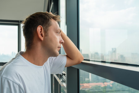 Unhappy frustrated man suffering from depression and bad news looking at window with city view....