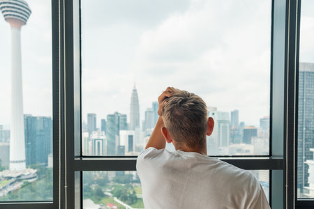 Rear view of unhappy frustrated man suffering from depression and bad news looking at window with...
