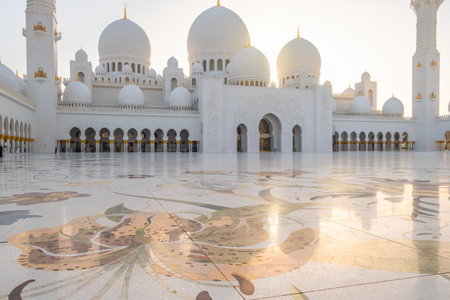 Courtyard of Sheikh Zayed Grand Mosque in Abu Dhabi, UAE with white marble domes, minarets and floral marble flooring at sunset. Islamic art and architecture. Popular Arabic landmarkの写真素材