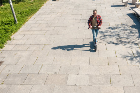 Man riding electric scooter in city public park at sunny summer day. High angle view from drone. Male driving e-scooter outdoors. Eco-friendly transport and travel. Sustainable lifestyle conceptの写真素材