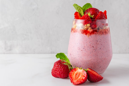 Strawberry chia pudding topped with fresh strawberries, granola and mint in a glass on white background. Strawberry yogurt with chia seeds. Healthy breakfast. Tasty foodの写真素材