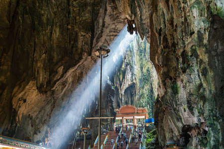 Batu Caves interior, Selangor, Malaysia. Tourists visiting Batu cave complex illuminated staircase with people by natural light streaming through the caves opening, Kuala Lumpur. Travel landmarkの写真素材
