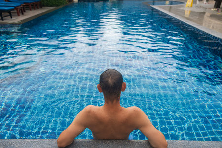 Back view of man relaxing in tropical resort swimming pool in the clear blue water on Phi Phi island, Thailand. Luxury travel and tourism. Tranquility, reflection and quiet relaxationの写真素材