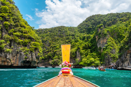 Front view from traditional Thai wooden long-tail boat with turquoise water and green cliffs on sunny day on Phi Phi islands, Krabi, Thailand. Sailing to Maya Bay beach. Travel and tourism in Asiaの写真素材