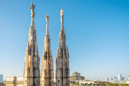 Spires of Gothic cathedral Duomo di Milano with statues and ornate decorations against clear blue sky and modern city skyline, Milan, Lombardia, Italy. Close upの写真素材