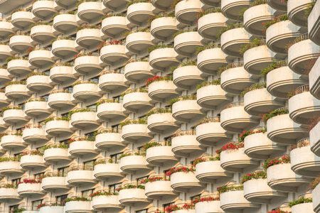 Repetitive pattern of rounded balconies on residential building facade with flower boxes and greenery, Bangkok, Thailand. Symmetry, geometric, minimalistic architecture backgroundの写真素材