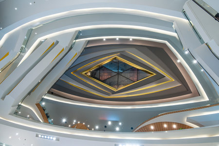 Upward view of modern shopping mall interior with futuristic architecture and layered geometric...