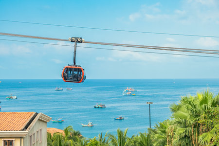 Modern cable car cabin ride over tropical seaside with fishing boats and blue ocean on Phu Quoc...