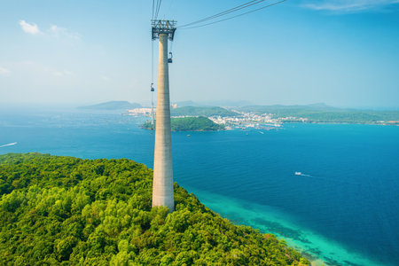 Cable car support tower rising above tropical green island forest with coastal town and turquoise sea. Longest Hon Thom cable car ride in the world on Phu Quoc island, Vietnam. Tourism technologyの写真素材