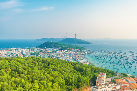 Aerial view of coastal town with dense green forest, fishing boats in blue sea and cable car stretching between islands on Phu Quoc island, Vietnam. Modern Hon Thom cable car systemの写真素材