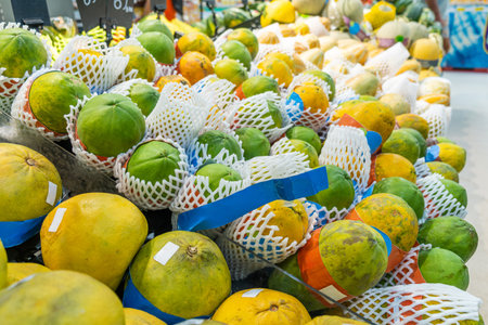 Fresh papayas and pomelos displayed in supermarket, wrapped in protective netting for sale in the fruit section. Freshness, abundance in grocery store in Thailand. Food retailの写真素材
