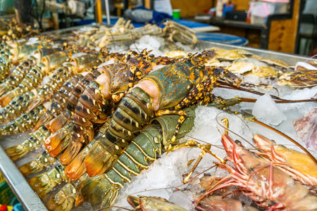 Fresh lobsters and tiger prawns displayed on crushed ice at the seafood counter in supermarket for sale. Giant shrimps cooling on the shelf of grocery store in Thailand. Food shopping and retailの写真素材