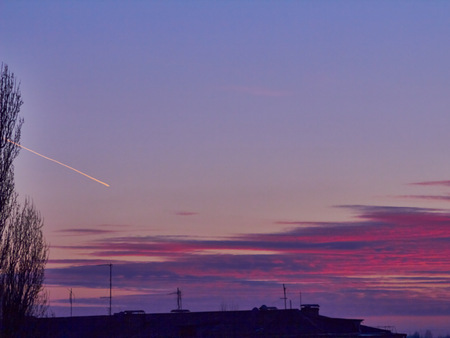 Sunset with red stratus clouds and blue sky with flying white plane