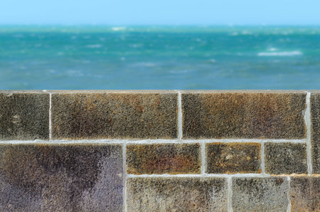Stone fence wall and greenish turquoise sea in the distanceの写真素材