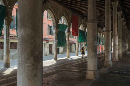 A big building with pillars and arches, and a woman  passing by in the distance, Venice, Italy.のeditorial素材
