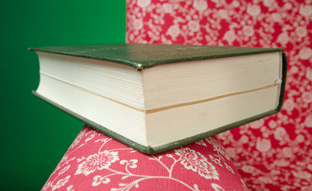 Closed book on red armchair rest left after reading, with green background.の写真素材