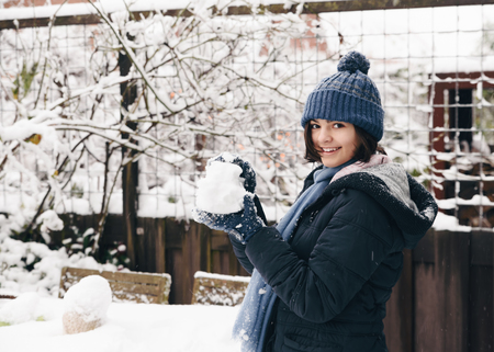 Little girl makes snowballs in a backyard, enjoying the first snow in late autumn.