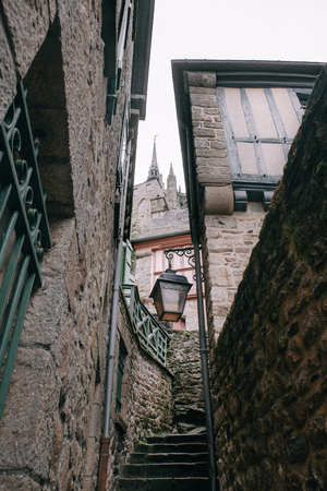 Stairs in a narrow street with stone houses and vintage lamp in Mont Saint Michel village center, in Normandy , Franceの写真素材