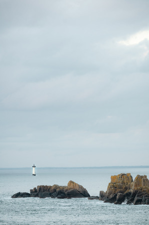 Cliffs with lighthouse in the distance, with rocks illuminated by sun rays just before sunset, Brittany, Franceの写真素材