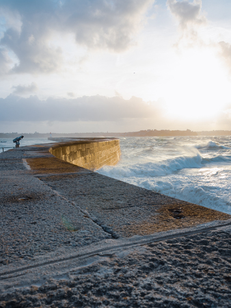 Big waves crushing on curved stone pier, on stormy weather with vivid sunset, big tide, Saint Malo, France.の写真素材