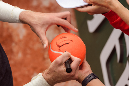 Tennis player signs autograph on a tennis ball after win, closeup photo showing tennis balls and hats and hands of a man making signature.のeditorial素材