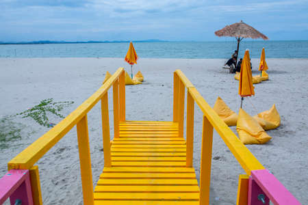 Yellow wooden stairs leading to the beach with umbrella and chair in the background