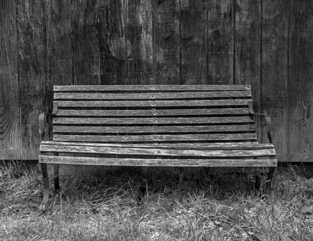 Black and white photo of the weathered lonely bench on the weathered wooden backgroundの写真素材