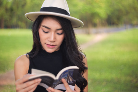 Attractive student teen girl reading book on green spring grassの写真素材