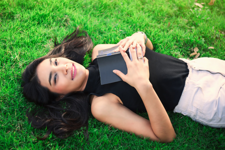 Attractive student teen girl reading book on green spring grassの写真素材
