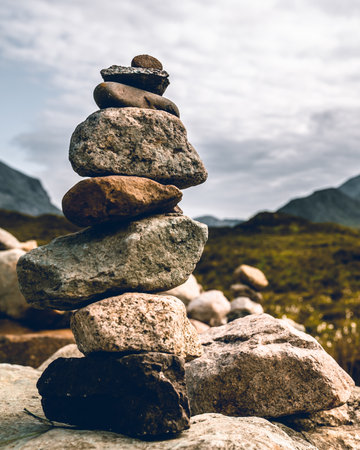 A trail winds through the Scottish Highlands, marked by a pile of rocks, creating a guide for hikers. These cairns, carefully stacked by previous adventurers, stand as silent sentinels, guiding the way amidst the vast and untamed beauty of the Highland landscapes, ensuring a safe passage through nature's rugged embrace.の写真素材