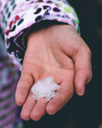 A hand emerges from a wintry landscape, delicately presenting a small mound of snow to the camera. The glistening crystals on the fingertips capture the enchantment of the moment, inviting viewers to embrace the fleeting beauty of nature's touch.の写真素材