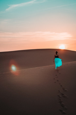 Elegant and ethereal, a woman in a blue skirt glides through a sand dune, a vision of grace amidst the textured desert backdropの写真素材