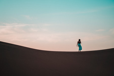 Elegant and ethereal, a woman in a blue skirt glides through a sand dune, a vision of grace amidst the textured desert backdropの写真素材