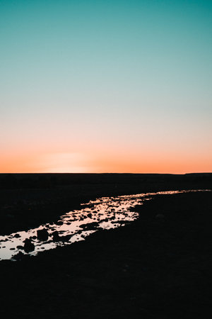 Golden hour river: A shimmering reflection of the setting sun transforms a river into a tranquil canvas of warm, golden hues, radiating serene beauty.の写真素材