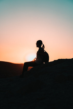 Sunset silhouette: A woman sits in graceful stillness, her silhouette capturing the tranquil beauty of the fading sun, a moment of serene contemplation.の写真素材