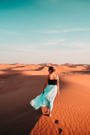 Elegant and ethereal, a woman in a blue skirt glides through a sand dune, a vision of grace amidst the textured desert backdropの写真素材
