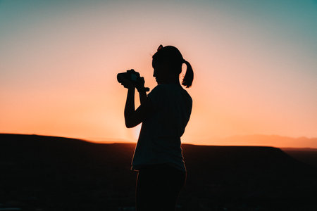 Sunset photographer: A woman's silhouette embraces the fading light, camera in hand, capturing the magic of the moment in a timeless frame.の写真素材