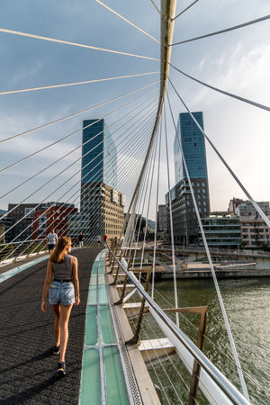 A woman gracefully crossing a modern bridge in Bilbao, the city's architectural marvel blending elegance and functionality.の写真素材